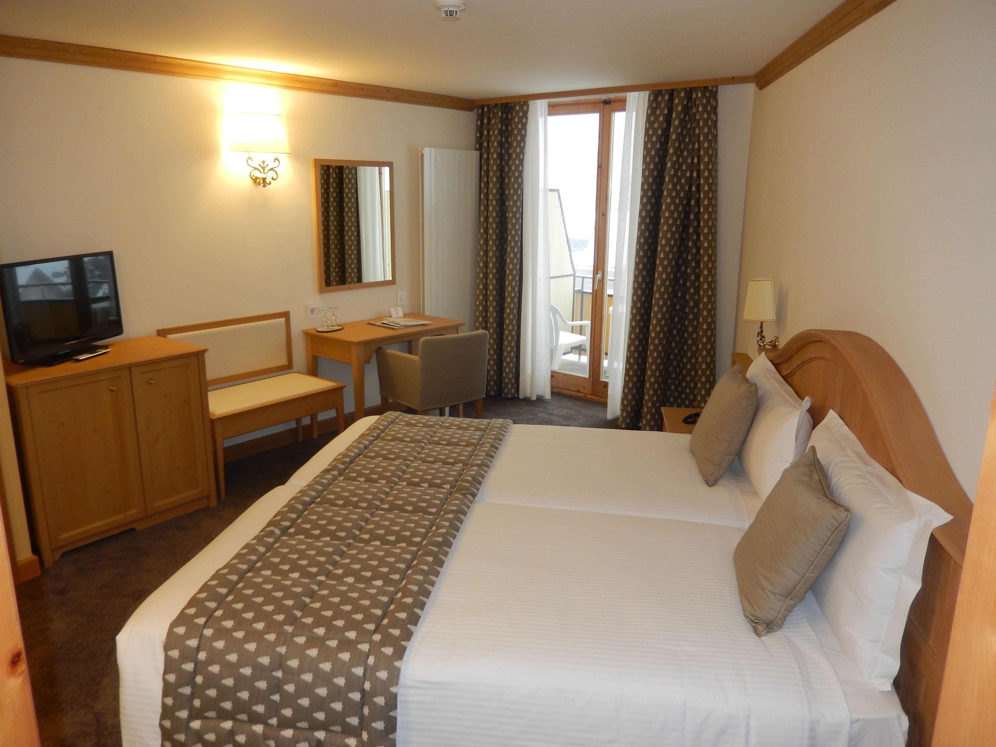 A hotel room with a bed, a desk, a chair, a television, and a window with curtains.