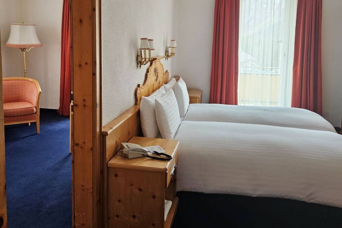 Une chambre d’hôtel avec un grand lit, une tête de lit en bois, deux tables de chevet, une lampe et une fenêtre avec des rideaux.