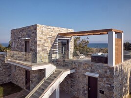 Una casa moderna con fachada de piedra, balcón de cristal y vista al mar.