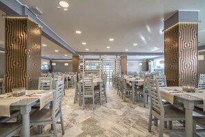 A spacious dining area with multiple tables and chairs, a patterned wall design, and a marble floor. - Golden Sun (Zakynthos)