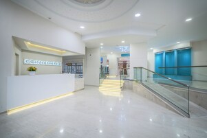 Zona de recepción de hotel con diseño moderno, que incluye un mostrador, una escalera y una barandilla de vidrio.