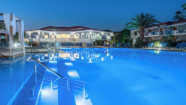 Piscina com superfície de água límpida, rodeada por espreguiçadeiras e um edifício com varandas.