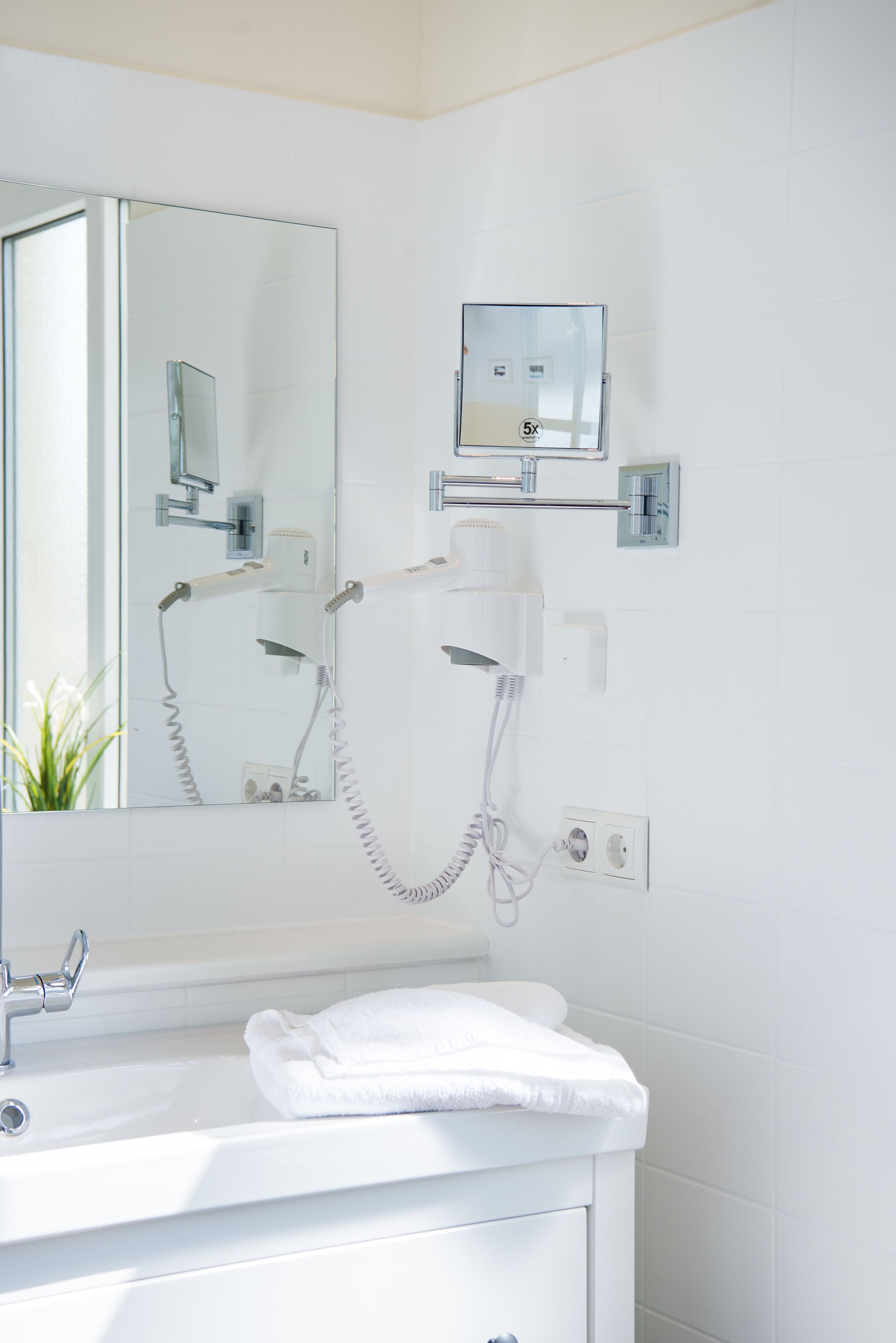A bathroom with a white sink, a mirror, a hairdryer, and a towel on the counter.