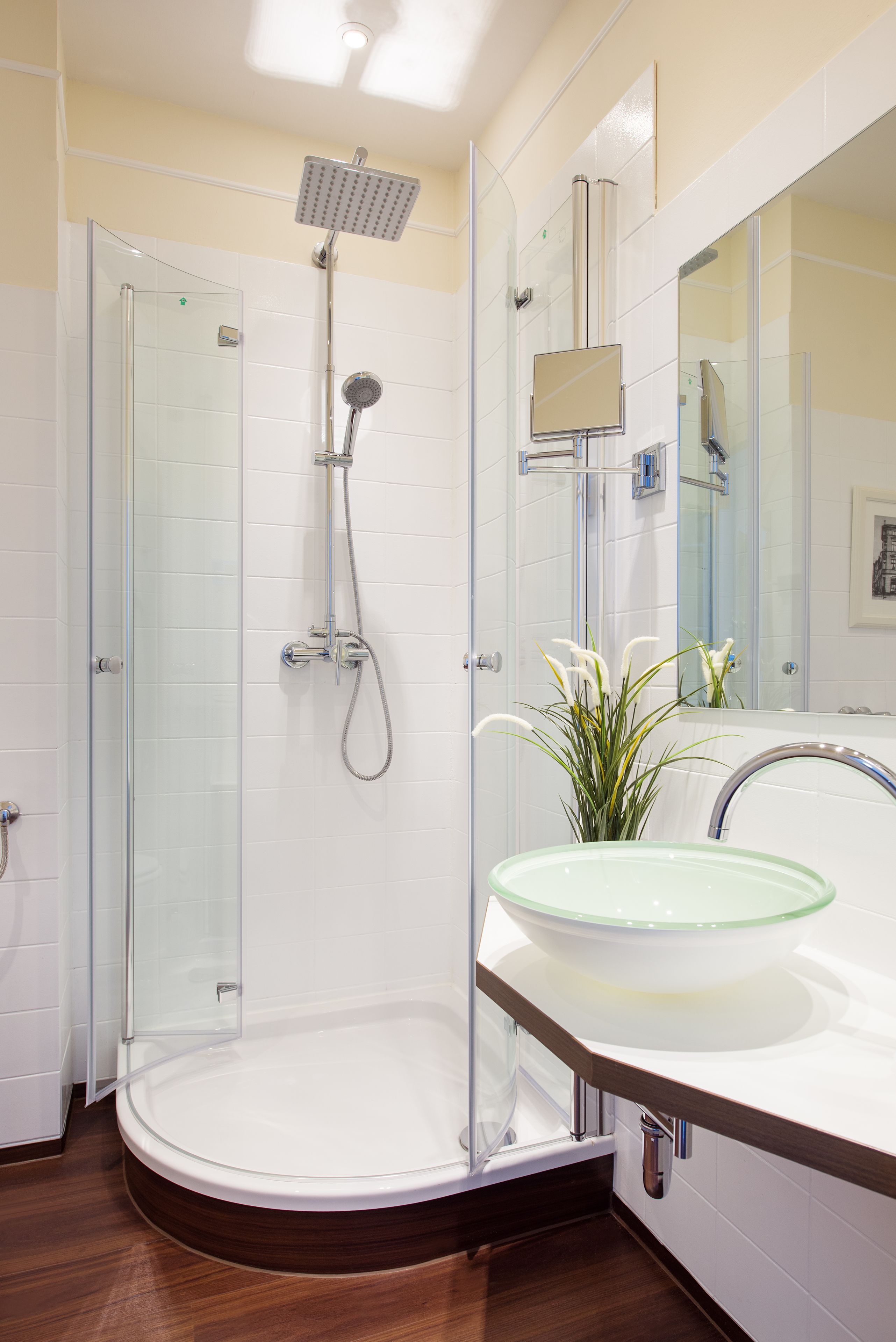 Un baño moderno con ducha de vidrio, lavamanos de vidrio y un espejo grande.