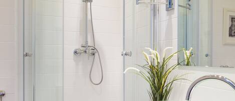 Un baño moderno con ducha de vidrio, lavamanos de vidrio y un espejo grande.