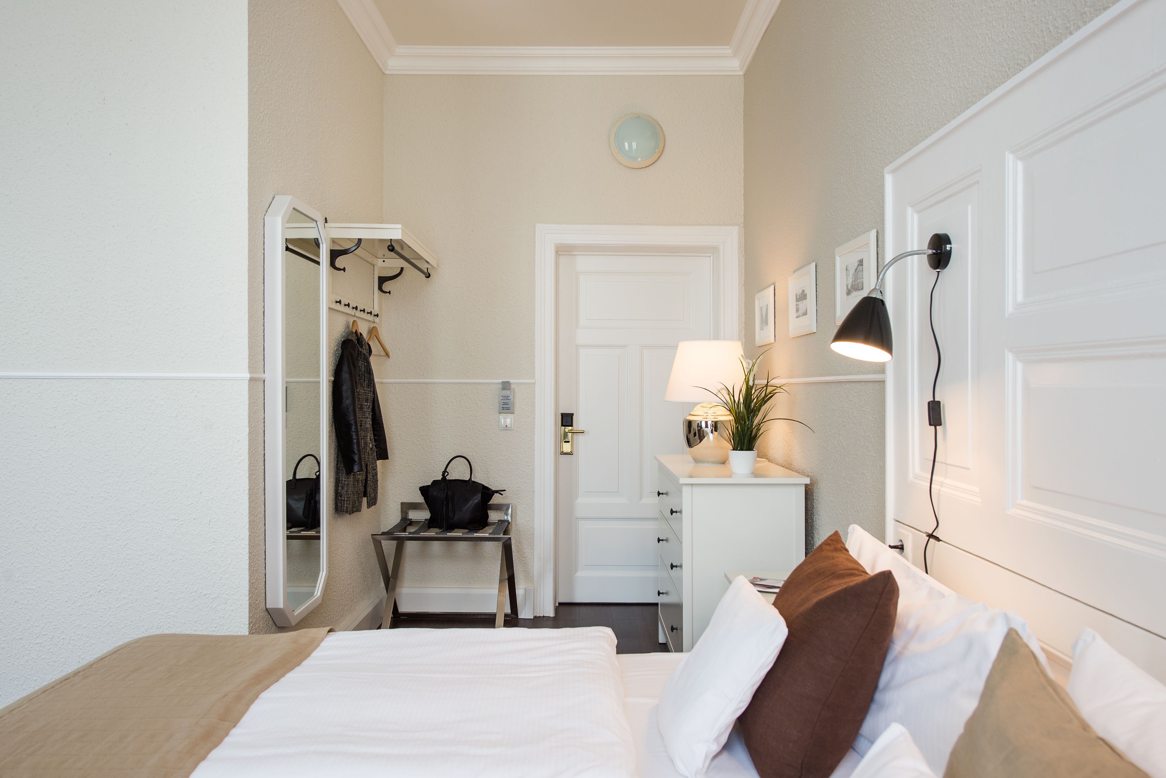 Ein Hotelzimmer mit Bett, Schreibtisch, Stuhl, Spiegel, Lampe und Kleiderständer.
