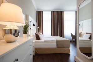 Quarto de hotel com cama, mesa de cabeceira, luminária, planta em vaso e um espelho grande.