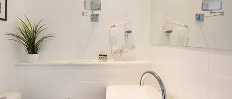 A modern bathroom with a white toilet, a sink with a mirror above it, and a potted plant on the counter.