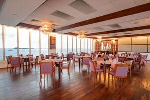 Un amplio comedor con suelo de madera y ventanas grandes que ofrecen vista al mar.