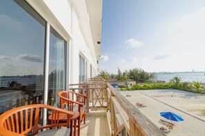 A balcony with wooden chairs and a table, overlooking a beach with a blue umbrella. - Hulhule Island Hotel- Private Beach Access & Airport Pick-up and Drop (Hulhulé)