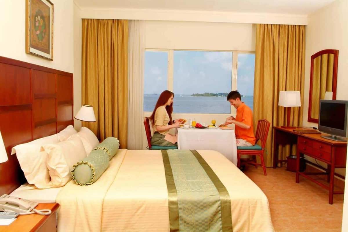 Ein Hotelzimmer mit Bett, Schreibtisch, Fernseher, Fenster mit Meerblick und Telefon auf dem Nachttisch.