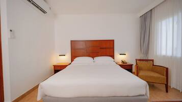 Een hotelkamer met een groot bed, een houten hoofdbord, bedlampjes, een stoel en een raam met gordijnen.