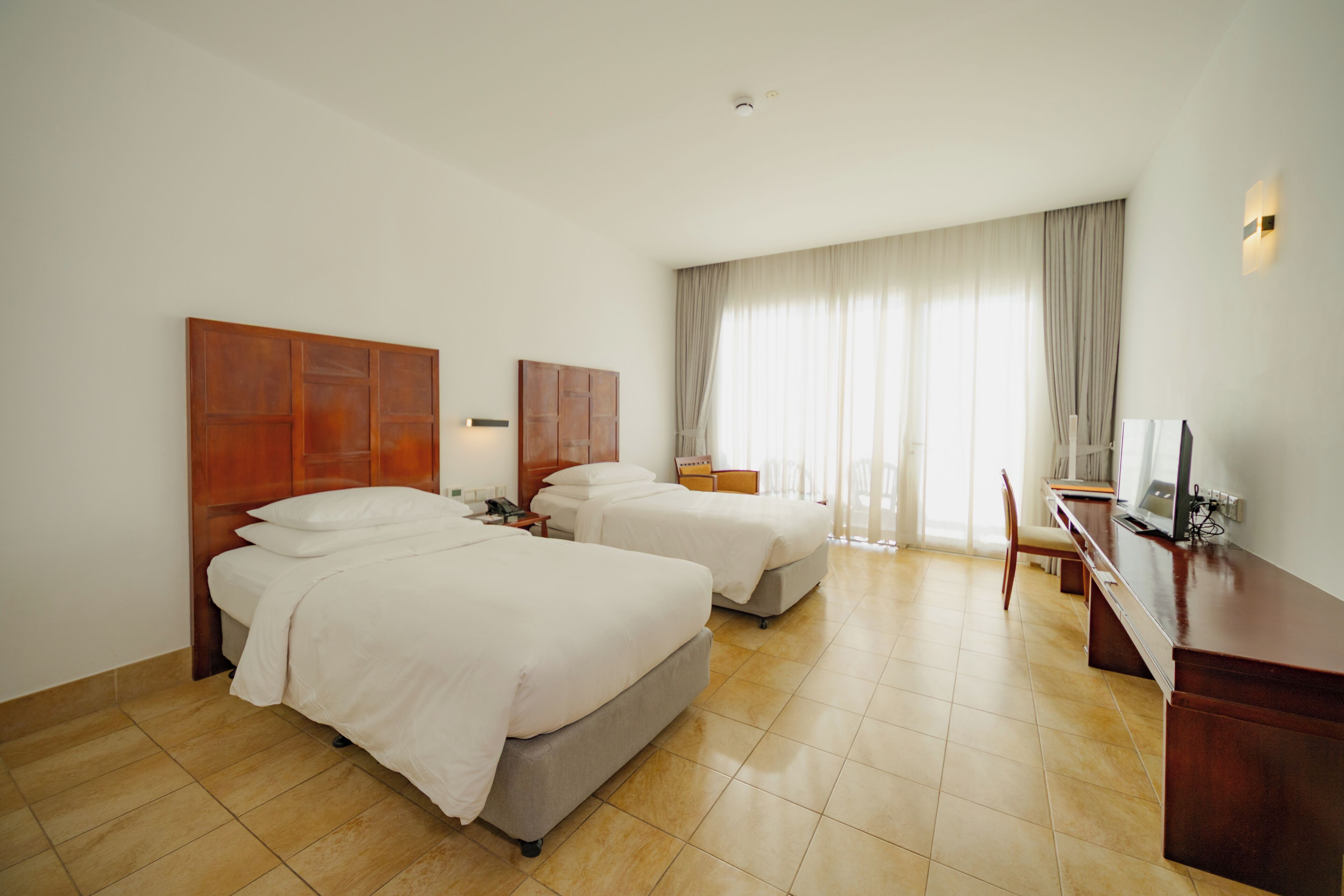 A hotel room with two beds, a desk, a chair, and a television.