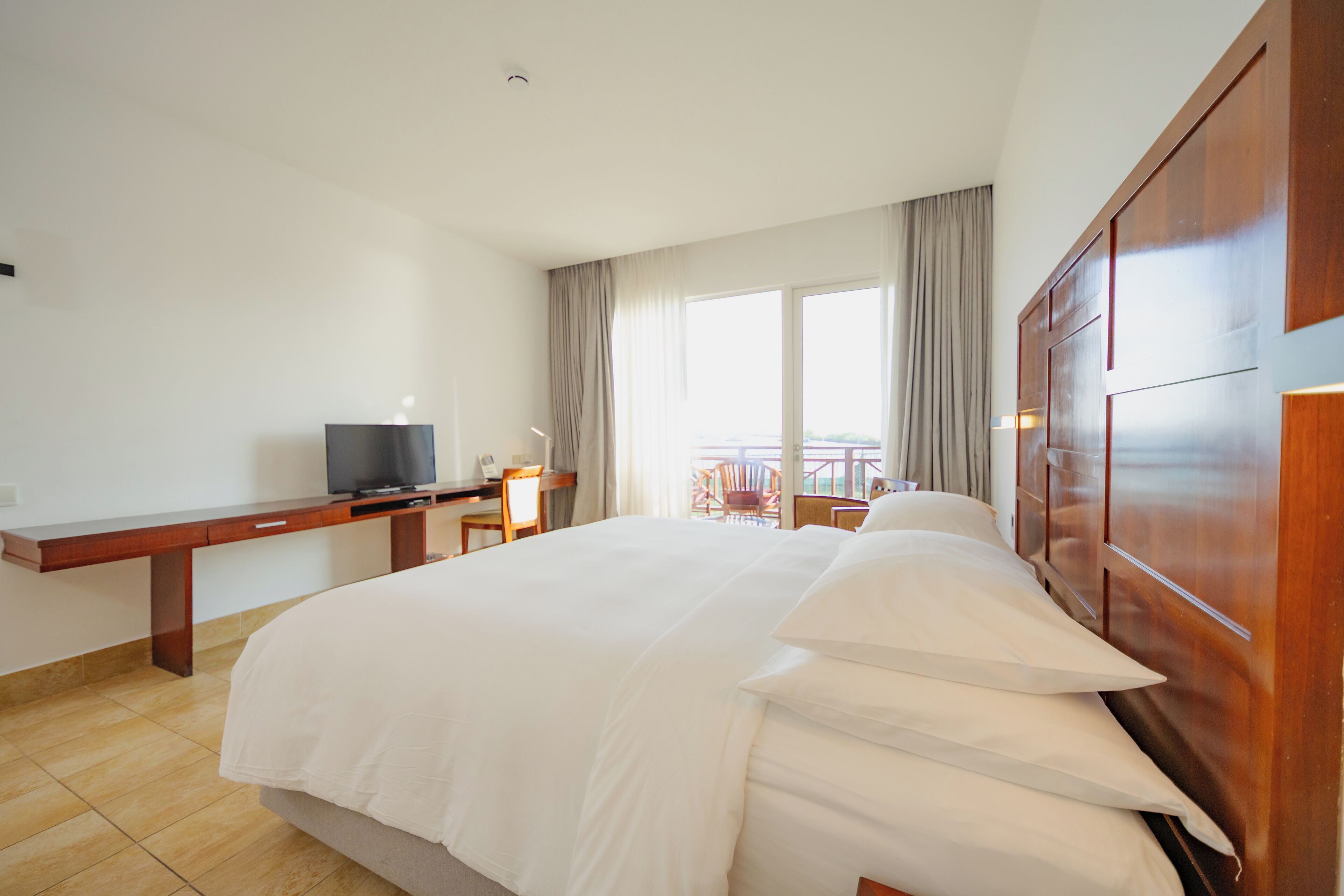 Una habitación de hotel con una cama grande, un escritorio con televisor y un balcón con sillas.