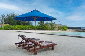 A beachside pool area with wooden lounge chairs and a blue umbrella. - Hulhule Island Hotel- Private Beach Access & Airport Pick-up and Drop (Hulhulé)