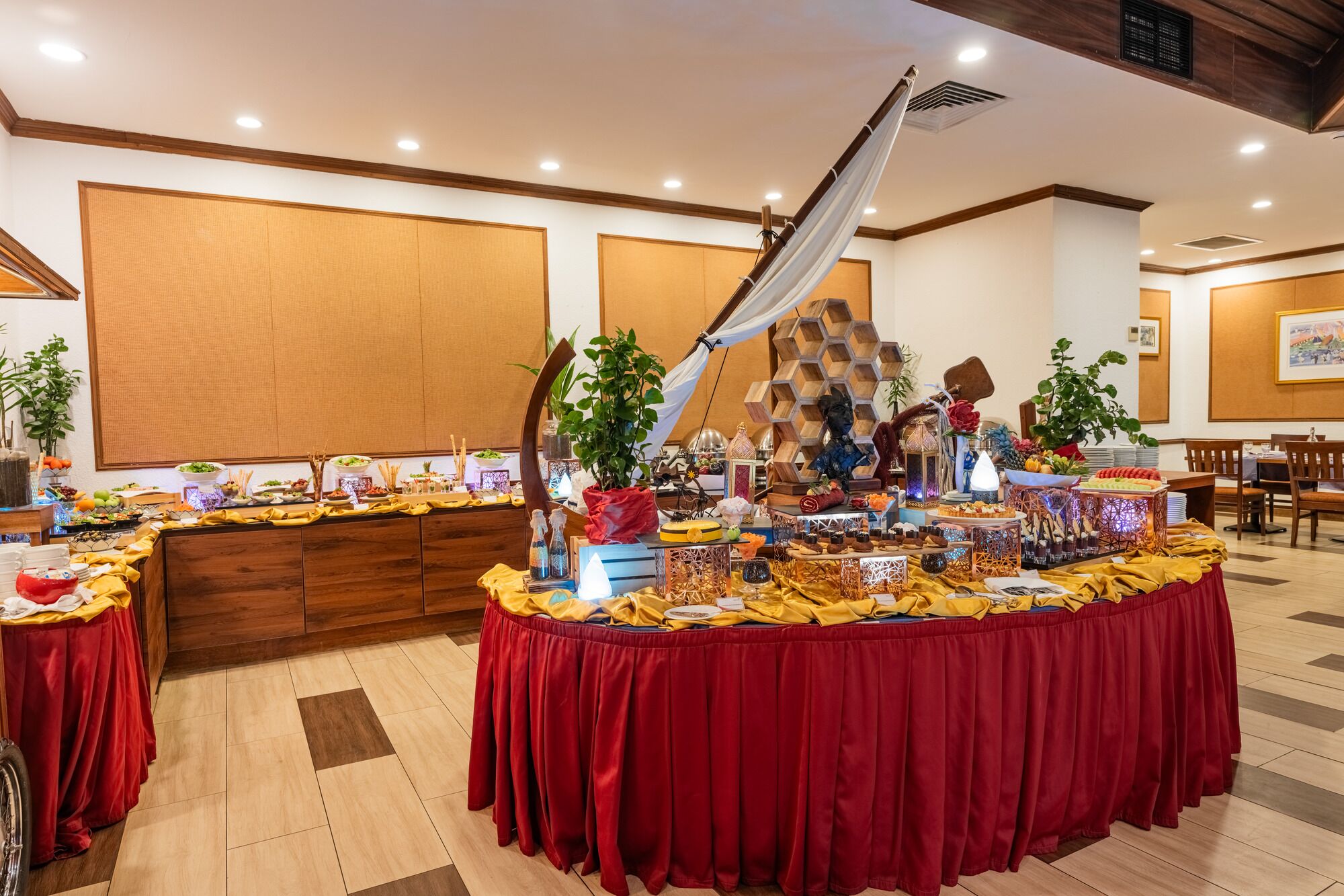 Disposição de buffet com diversos alimentos e decorações, incluindo uma planta grande e um arco decorativo.