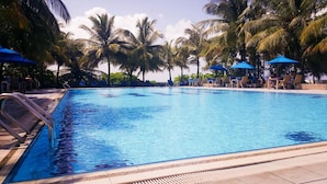 Una piscina con sillas de descanso y sombrillas, rodeada de palmeras.