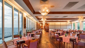 Un restaurante con varias mesas y sillas, ventanas amplias con vista al mar y suelos de madera.