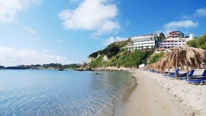 A beach with clear water, a sandy shore, and a building with multiple balconies overlooking the beach. - Palazzo di Zante (Zakynthos)