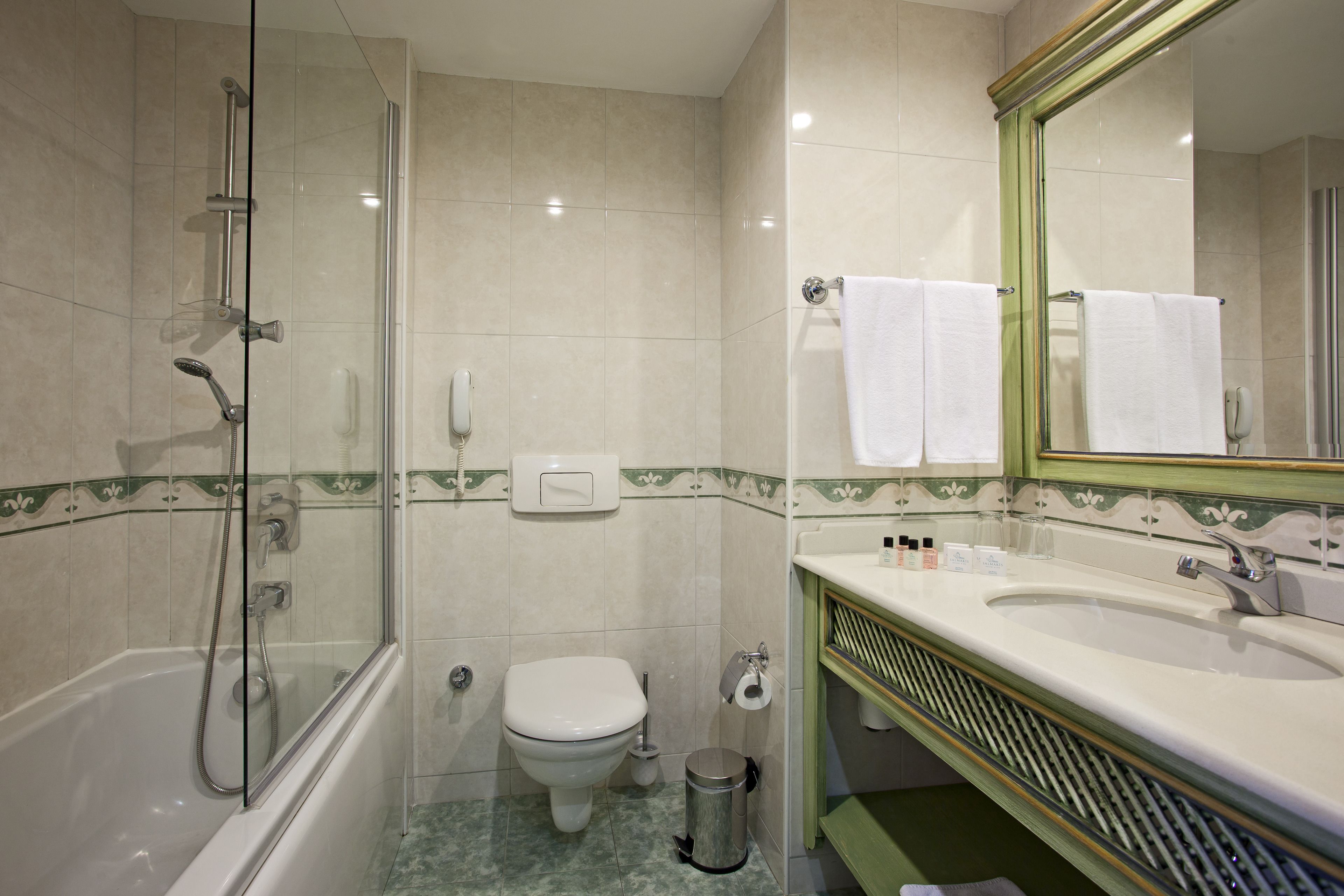 Un baño con ducha de vidrio, inodoro, lavamanos con espejo y cubo de basura.