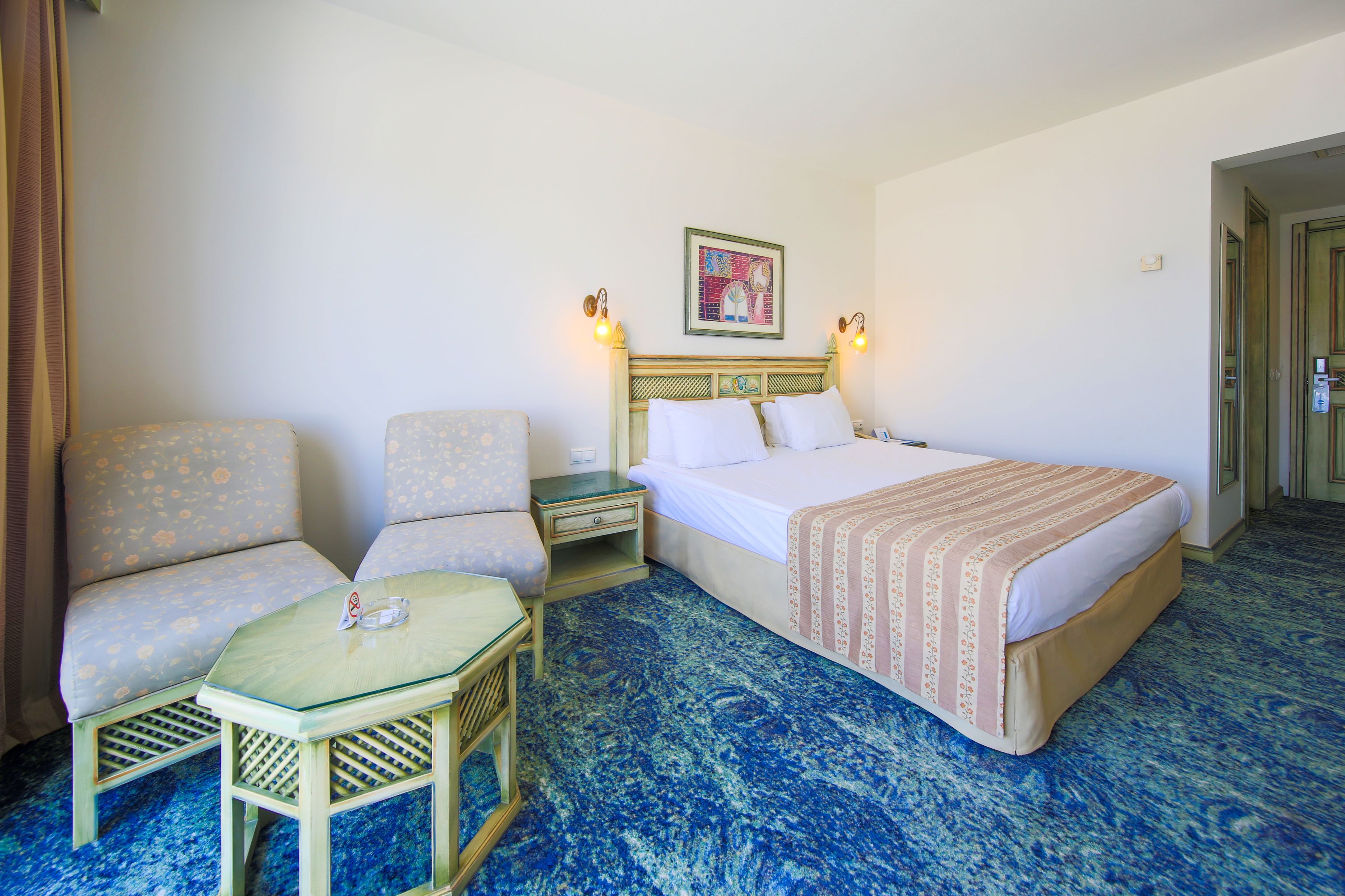 Una habitación de hotel con una cama, dos sillones, una mesita y una mesita de noche.