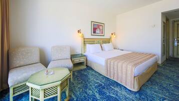 Una habitación de hotel con una cama, dos sillones, una mesita y una mesita de noche.