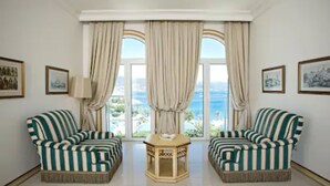 Una habitación con dos sofás a rayas frente a una mesa, ventanas grandes con cortinas y cuadros en las paredes.