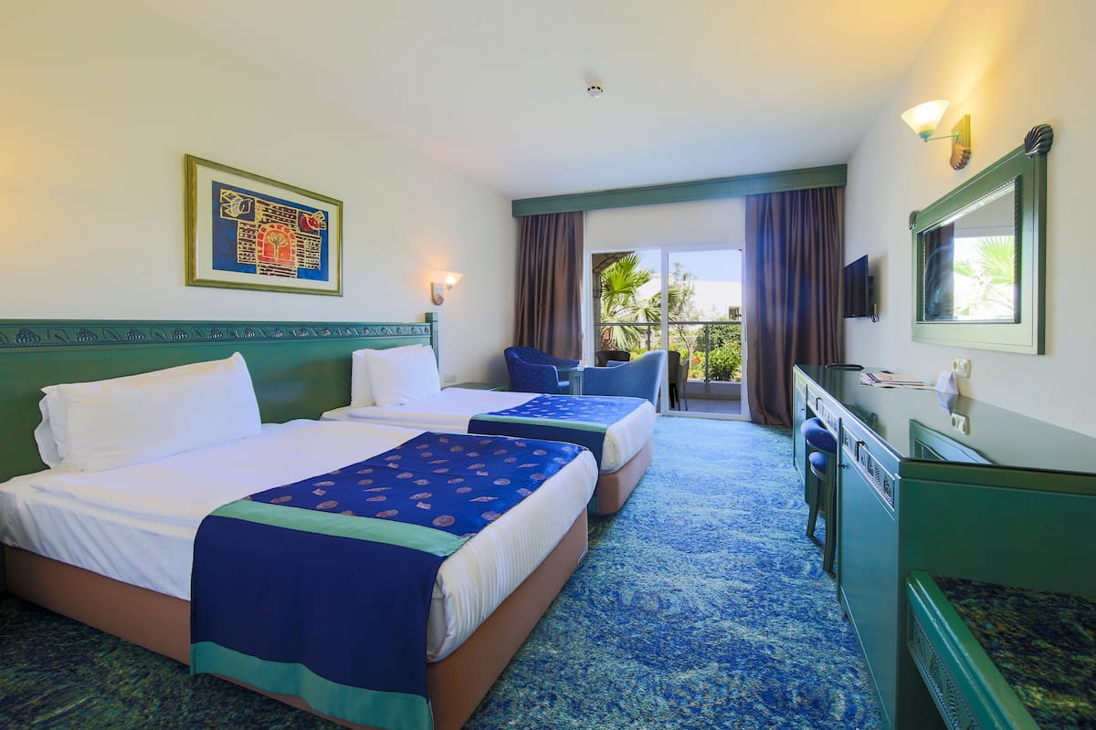 A hotel room with two beds, a desk, a chair, a television, and a balcony with curtains.