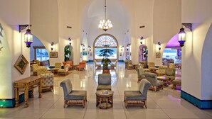 Un vestíbulo espacioso con techos altos, candelabros elegantes y un amplio ventanal con vistas a un paisaje tropical.