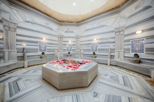 Un spa lujoso con una bañera de hidromasaje central, paredes de mármol y detalles en azulejos decorativos.