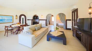 A living room with a sofa, dining table, chairs, a TV, and a kitchen in the background.