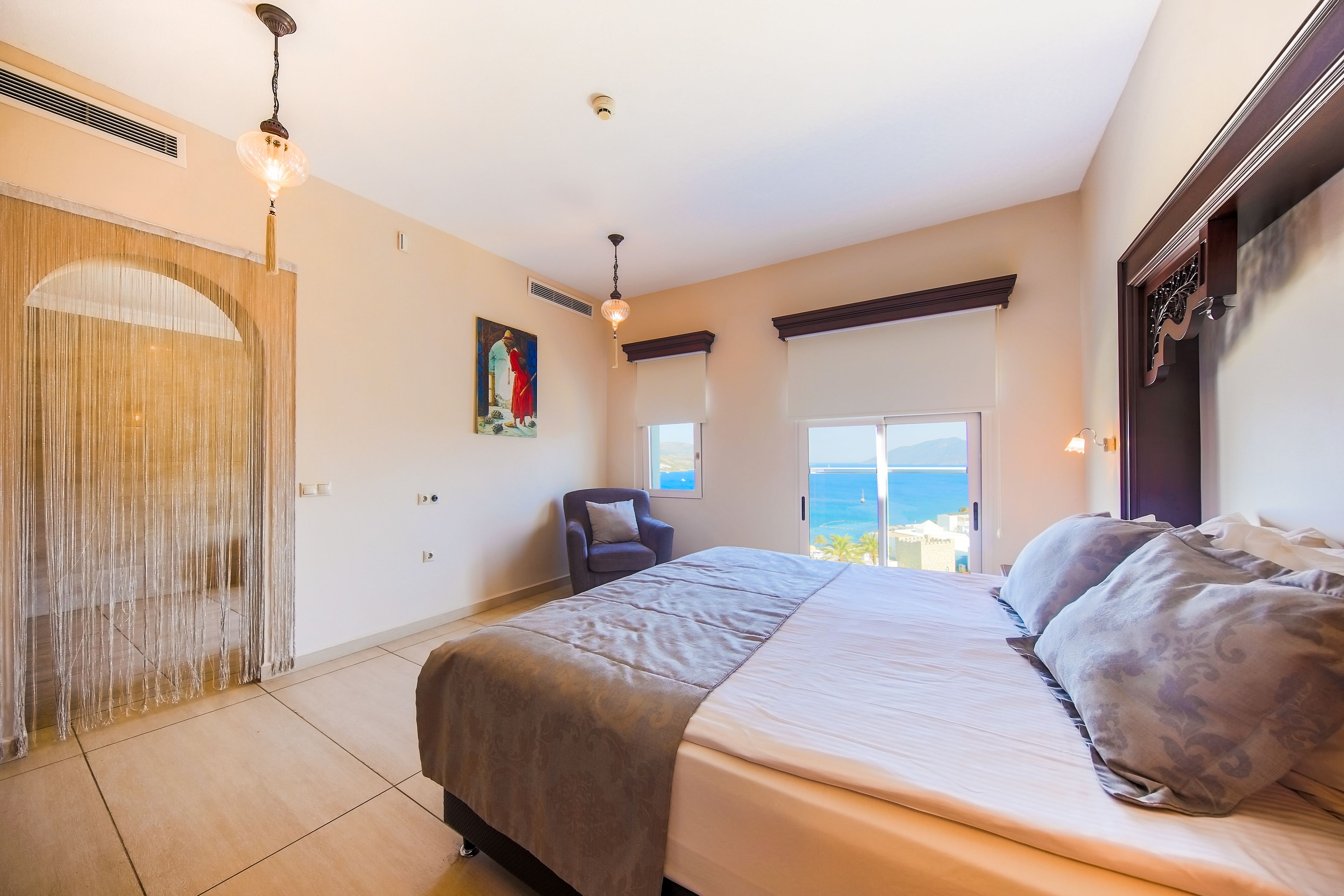 Une chambre à coucher avec un grand lit, une chaise, une fenêtre donnant sur un beau paysage et un élément décoratif mural.