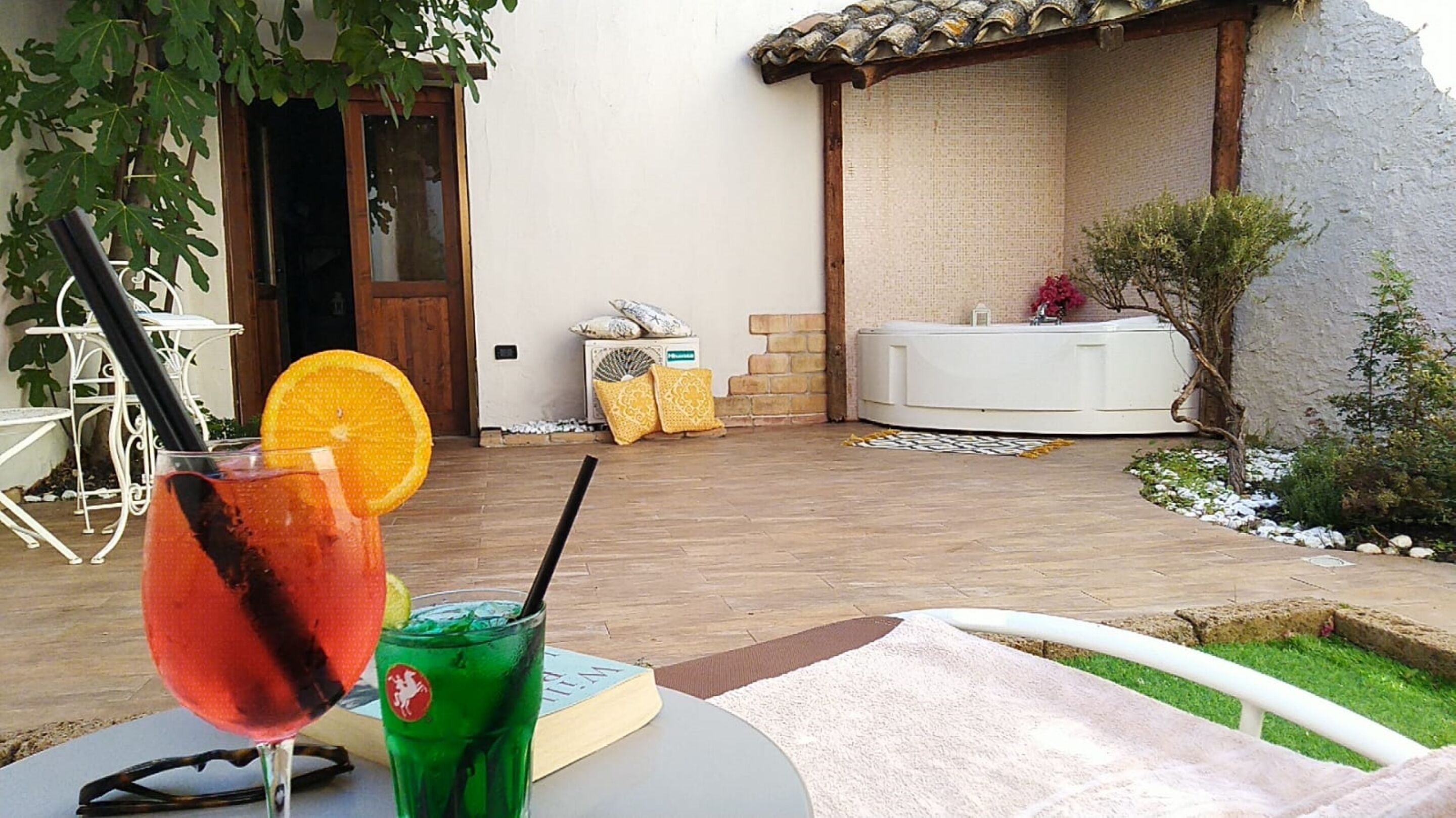 Eine Terrasse mit Tisch, Getränken, einem Stuhl, einem weißen Stuhl, einem kleinen Garten und einem Whirlpool.