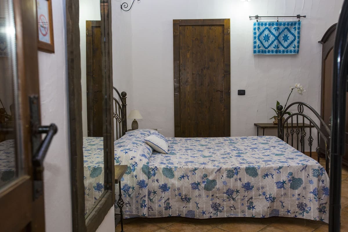 Une chambre avec deux lits, une porte en bois, une décoration murale bleue à motifs et une petite table sur laquelle est posé un vase.