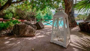 A white lantern on a concrete path with a pool and trees in the background. - Hotel Il Monastero (Quartu Sant'Elena)