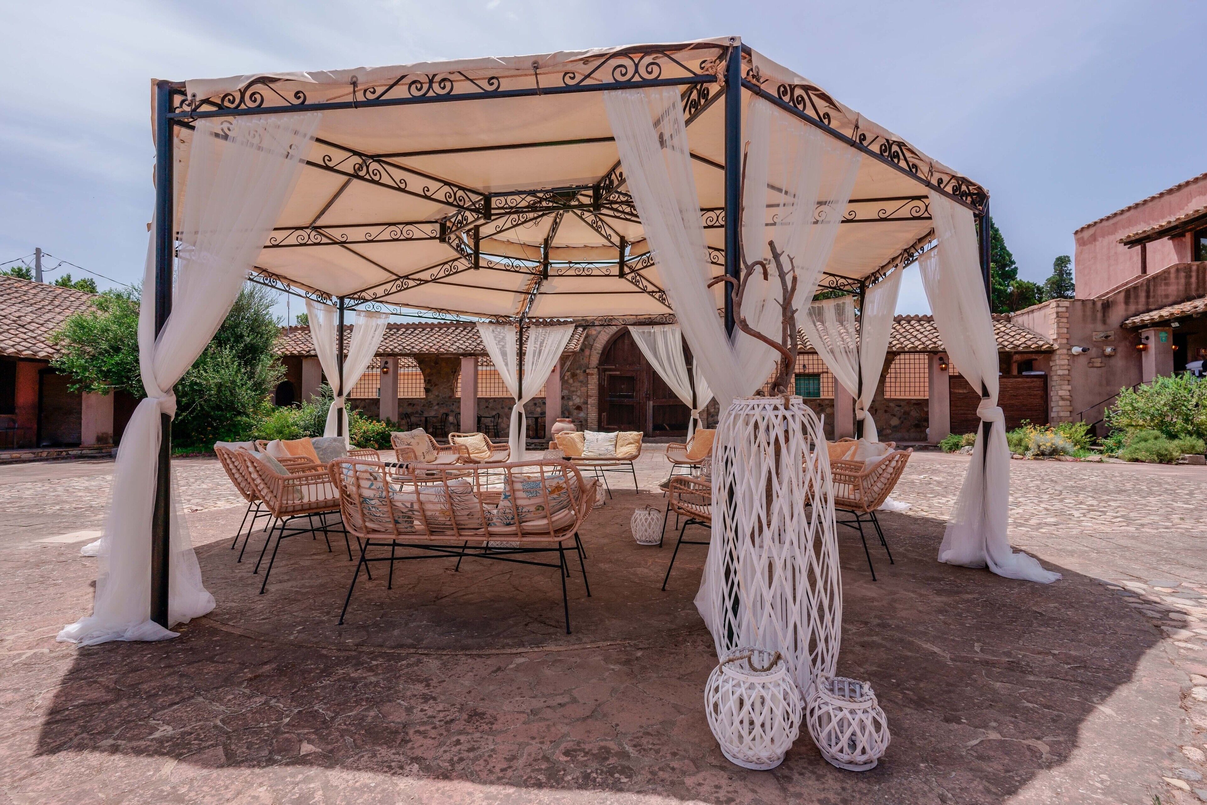 A covered outdoor seating area with wicker furniture and white drapes.