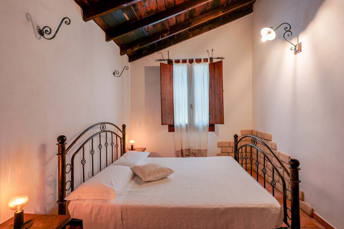 Une chambre à coucher avec un cadre de lit en bois, une table de chevet avec une lampe, une fenêtre avec des volets en bois et un escalier.
