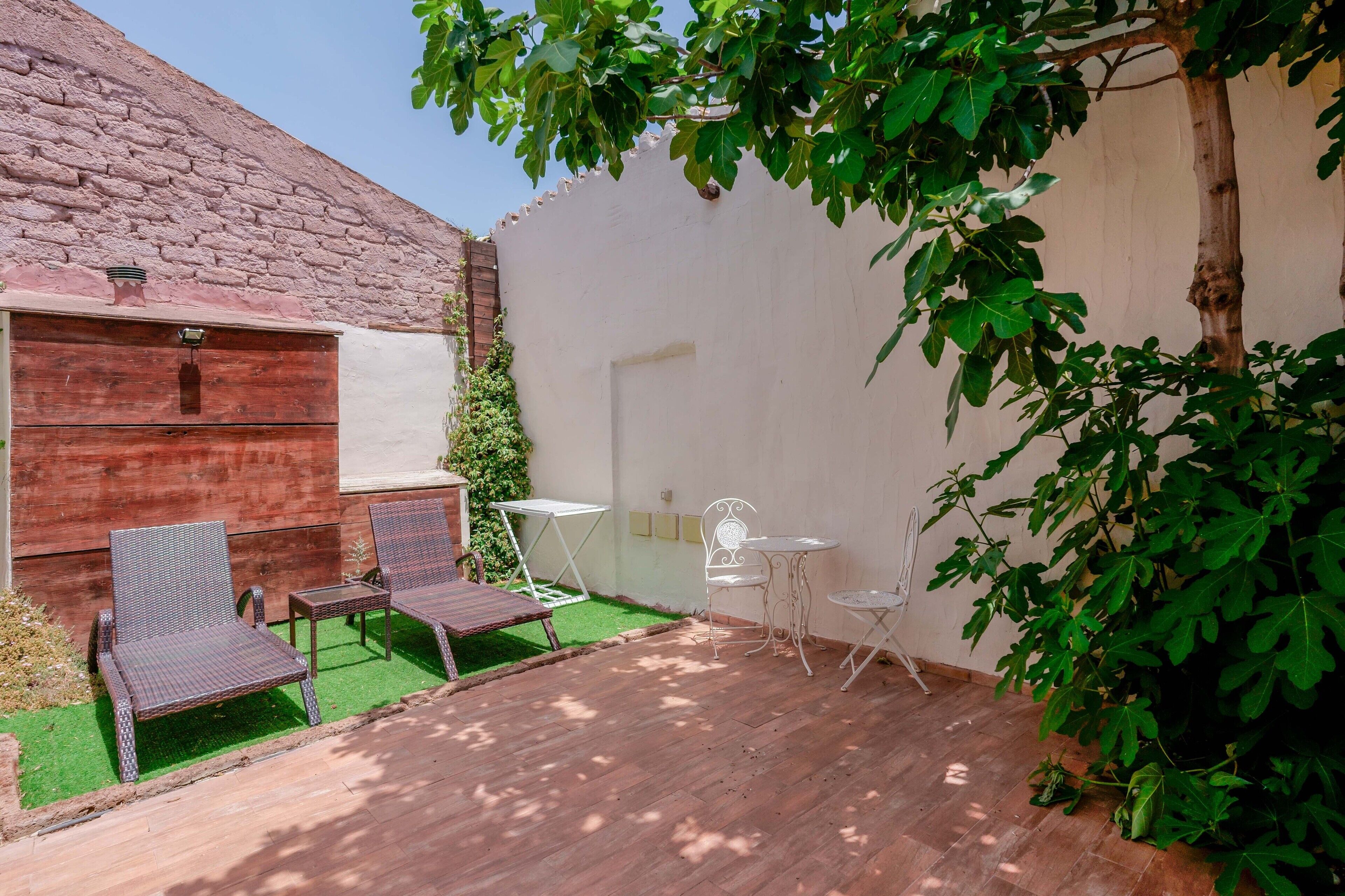 A patio with wooden flooring, two wicker chairs, a small table, and a white chair.