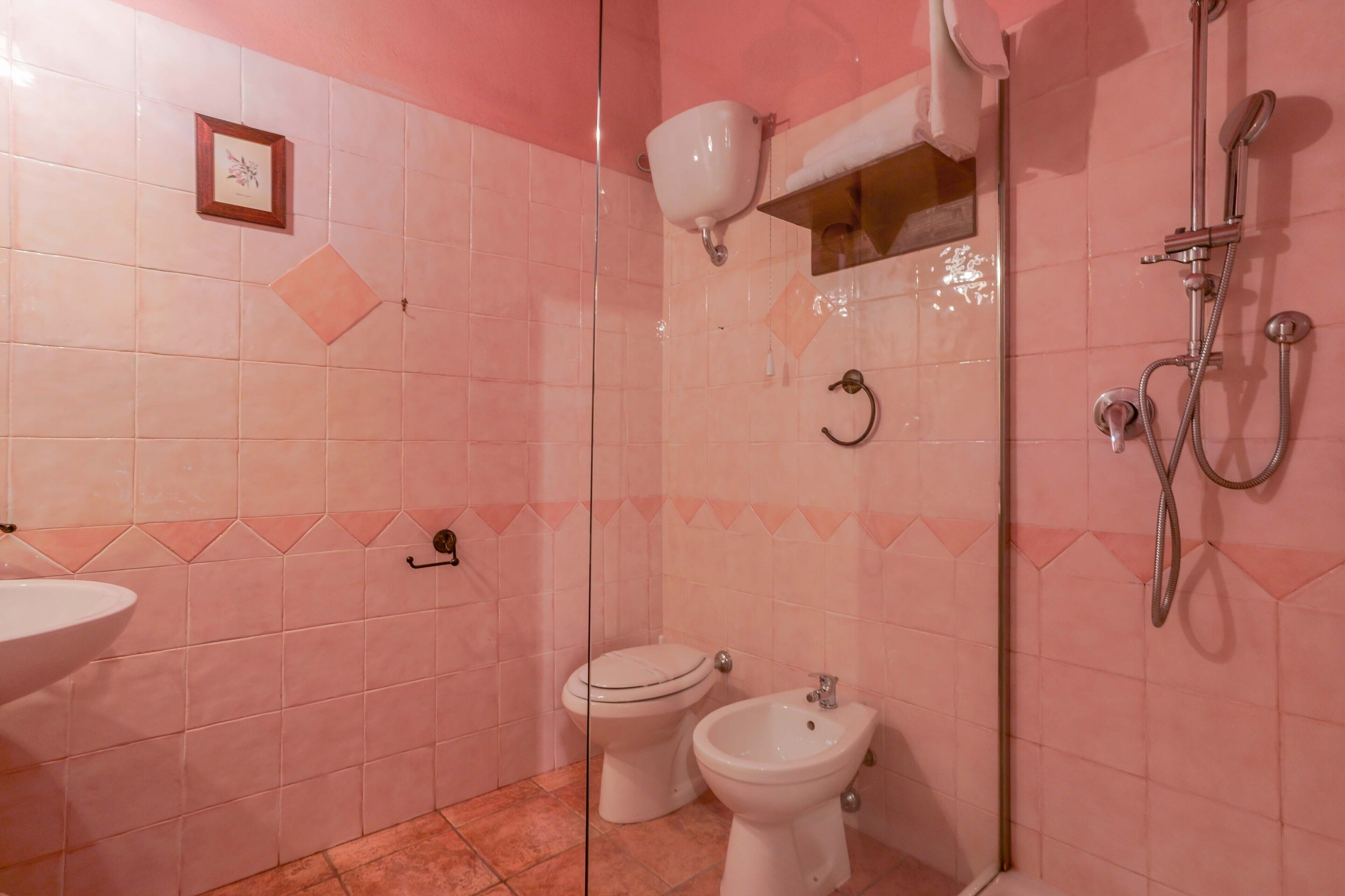 Un baño con azulejos rosa, un inodoro, un bidé, un lavabo y una ducha.