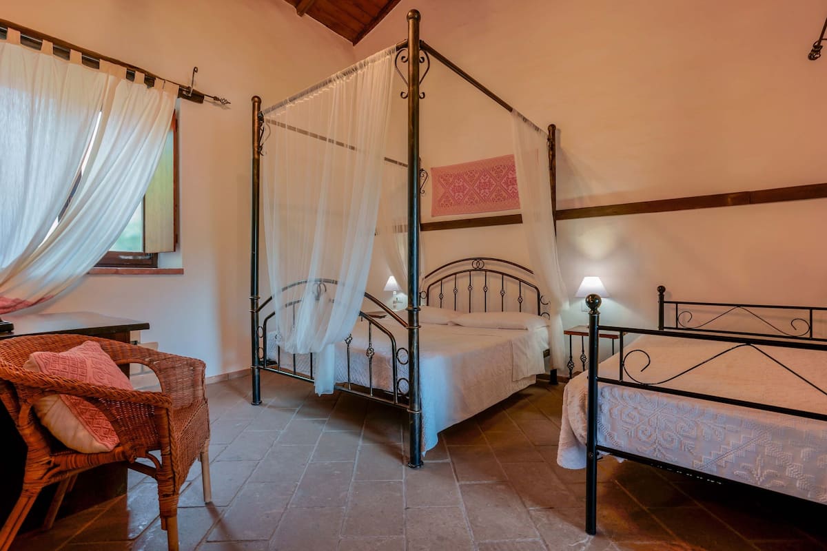 Un lit à baldaquin, une chaise en osier et un lit plus petit avec un cadre en métal.