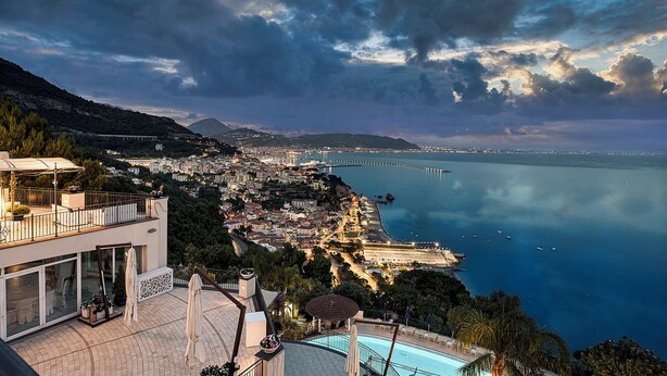 A coastal cityscape with a view of the sea, a bridge, and a swimming pool area.
