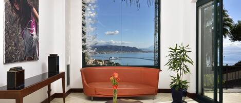 A modern living room with a large window, a sofa, a coffee table, and a potted plant.
