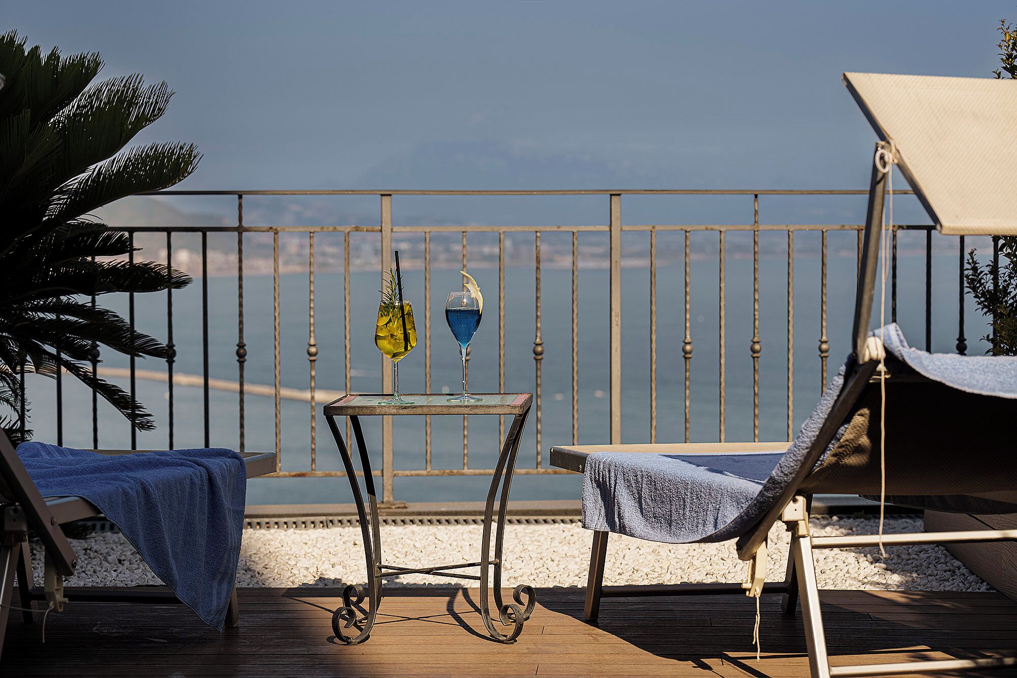 Eine Terrasse mit Tisch und zwei Stühlen, einem Geländer und Blick aufs Meer.