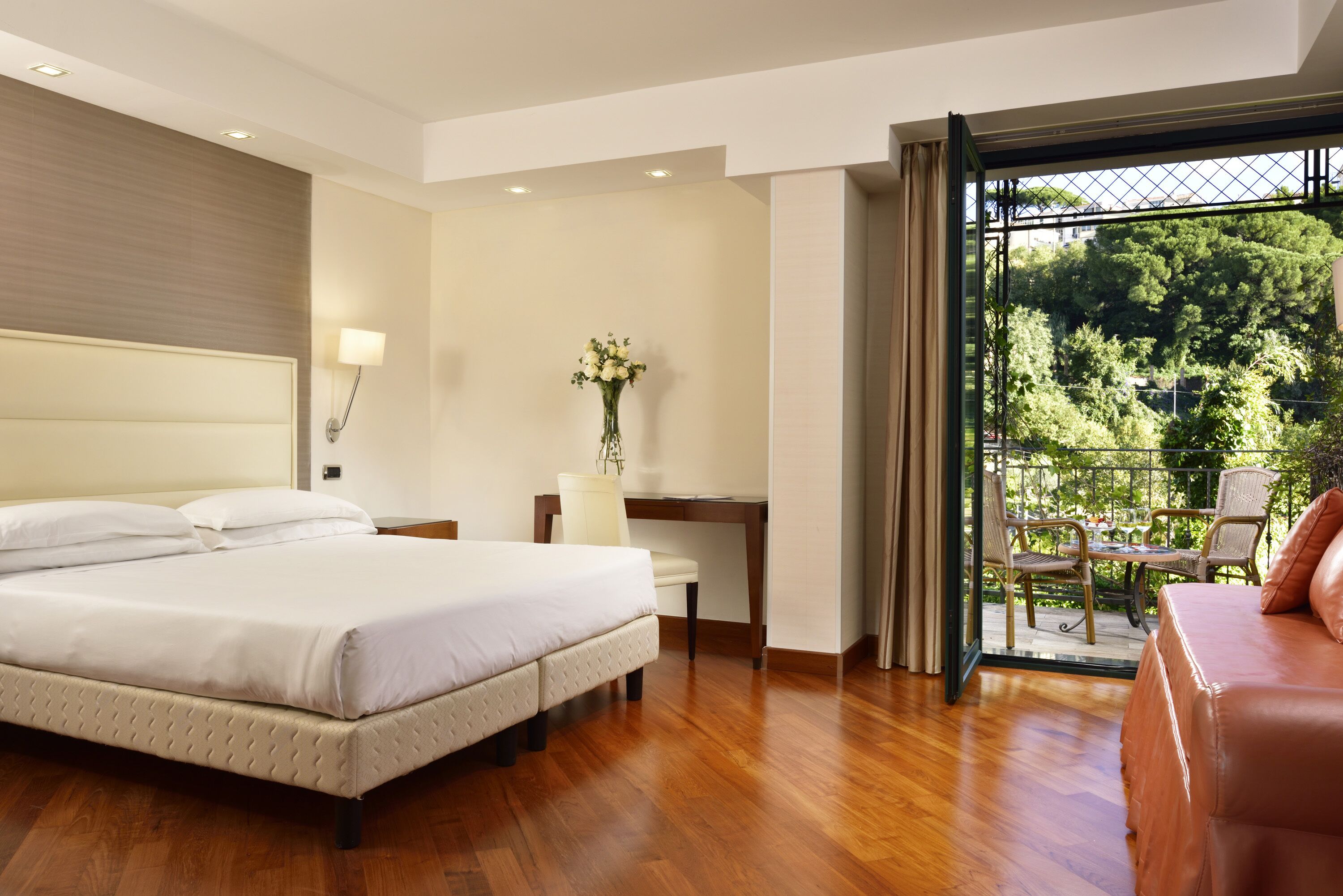 A hotel room with a bed, desk, and balcony with outdoor furniture.