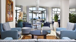 A modern living room with a view of the sea, featuring blue sofas, a round coffee table, and a large painting on the wall.