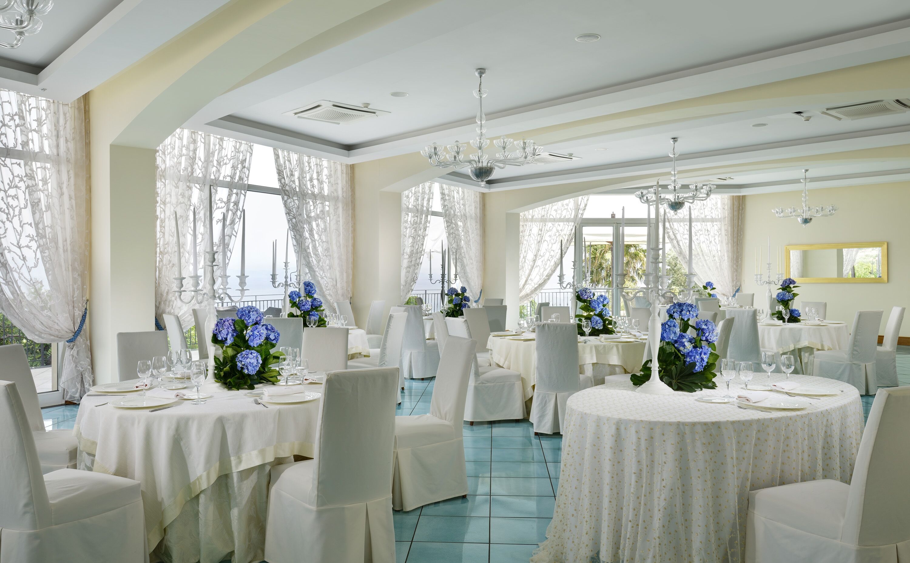 A formal dining room with white tables, chairs, and blue flowers.