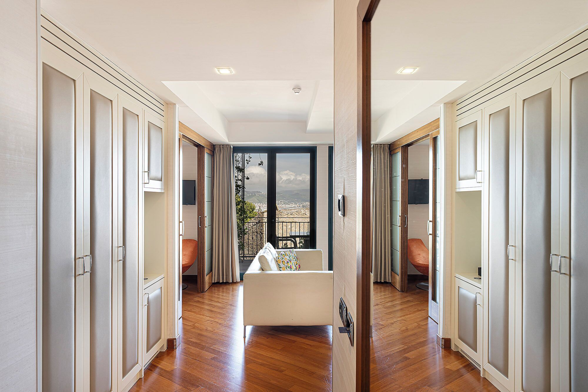 Un pasillo con vistas a un balcón, suelo de madera y muebles de cocina blancos.