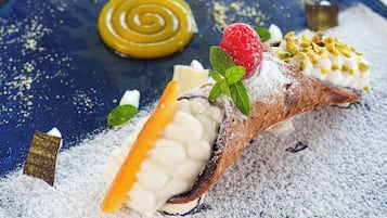 A dessert with a scoop of ice cream, a strawberry, and a mint leaf on top, dusted with powdered sugar.
