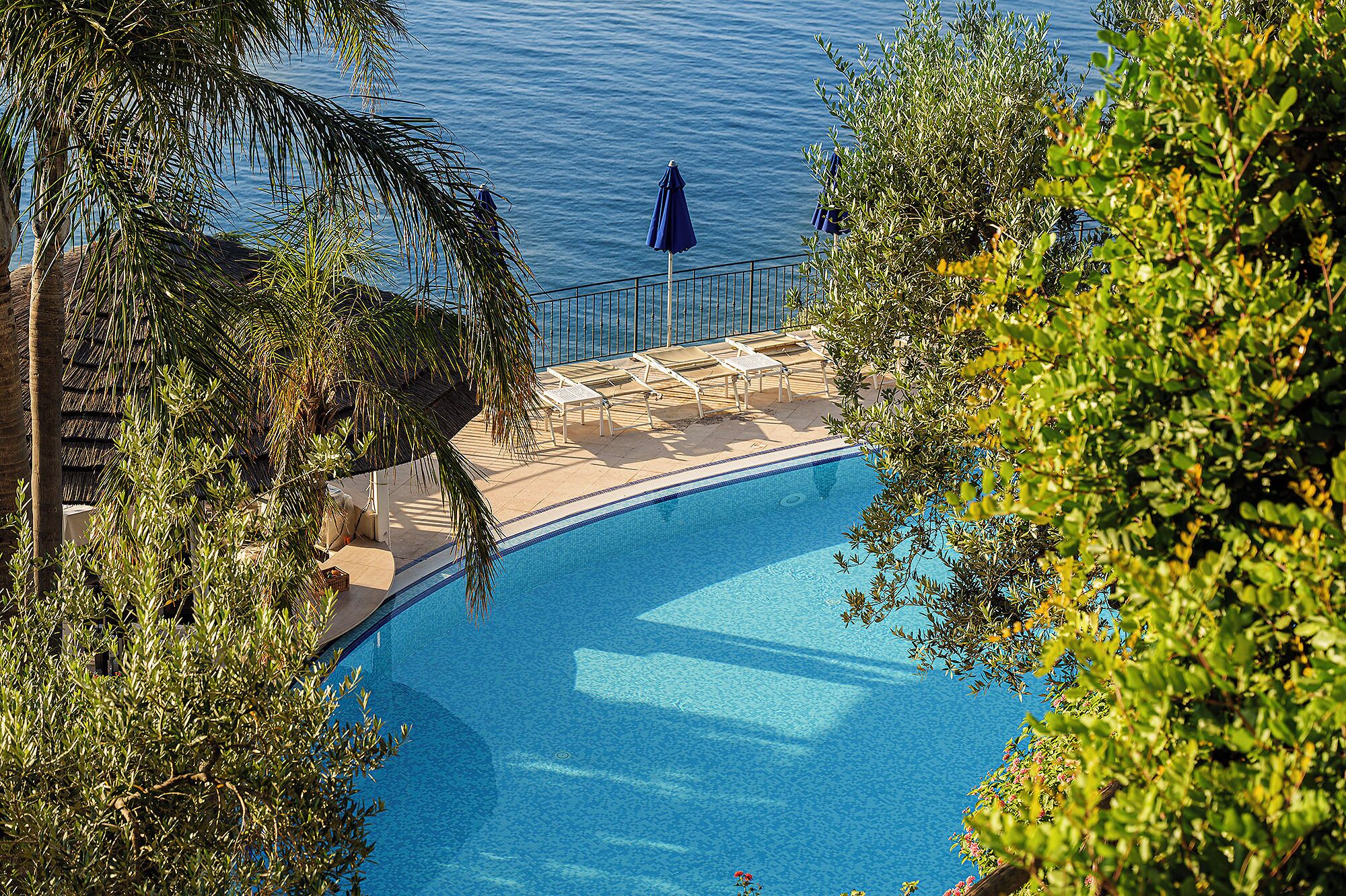 Piscina com vista para o mar, rodeada por vegetação.