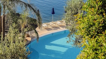 Piscina com vista para o mar, rodeada por vegetação.